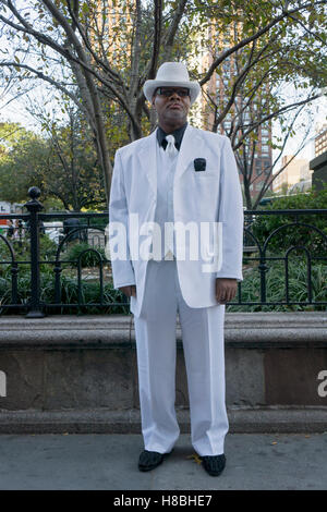 A stylish man in a white suit, tie & hat wearing a black shirt. In Union Square Park in New York City. Stock Photo