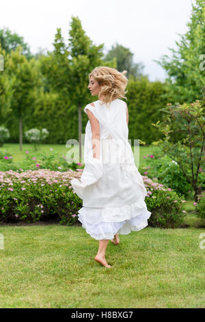 Happy young blonde woman walking barefoot on the green grass Stock Photo