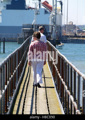 Middle aged couple walking along wooden jetty at Southampton Sailing Club, Woolston, Southampton, Hampshire UK Stock Photo