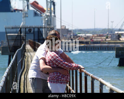 Middle aged couple cuddling and looking out to sea wooden jetty at Southampton Sailing Club, Woolston, Southampton, Hampshire UK Stock Photo