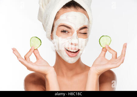 Young woman with clay facial mask holding cucumber slices isolated on white background Stock Photo