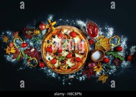 Homemade pizza with ham, mozzarella and cherry tomatoes on a black background. Top view. Stock Photo