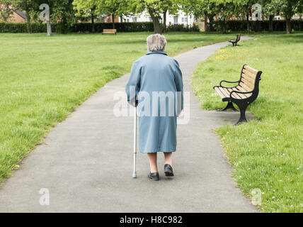 Ninety year old lady walking with stick in public park. England. UK Stock Photo