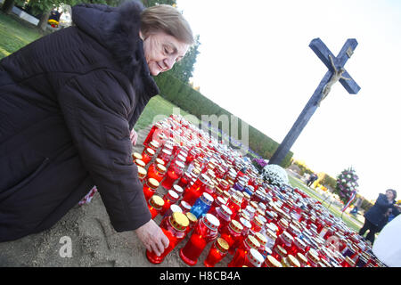 A woman putting a candle in front of the cross with a group of lampions lined up on the ground at cemetery on All Saints Day. Stock Photo