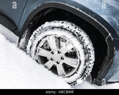 Modern blue car fragment, wheel with studded tire standing on winter road with deep snow Stock Photo