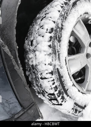 Car wheel with studded tire standing on winter road with deep snow, closeup photo with selective focus Stock Photo