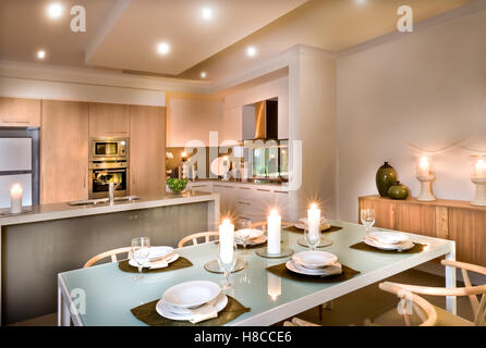 Modern kitchen and the dining room with candles everywhere, glasses and dishes on the shiny table, traditional meals serving. Stock Photo