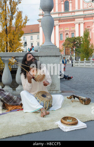 Indian man sat on rug, singing and playing Iktara (or ektara) - single string instrument, at Triple Bridge, Ljubljanica River, L Stock Photo