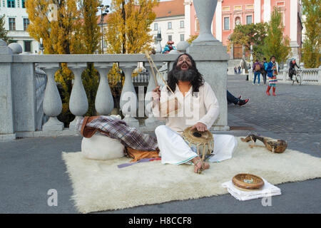 Indian man sat on rug, singing and playing Iktara (or ektara) - single string instrument, at Triple Bridge, Ljubljanica River, L Stock Photo