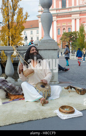 Indian man sat on rug, singing and playing Iktara (or ektara) - single string instrument, at Triple Bridge, Ljubljanica River, L Stock Photo