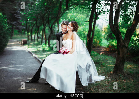 Bride and groom sitting on bench Stock Photo