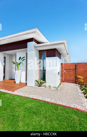 The lawn has very thin green grasses in front of the house, a yard made by stone and concrete from the right side. Sky is blue. Stock Photo