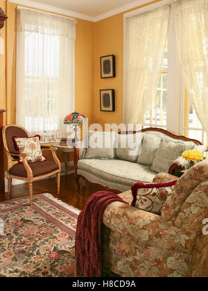 Yellow sitting room with upholstered sofa and floral patterned rug.. Stock Photo