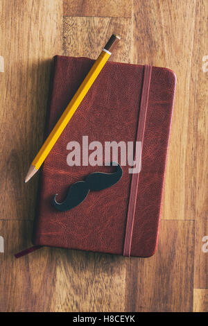 Fake black mustache on diary with pencil. Top view. Stock Photo