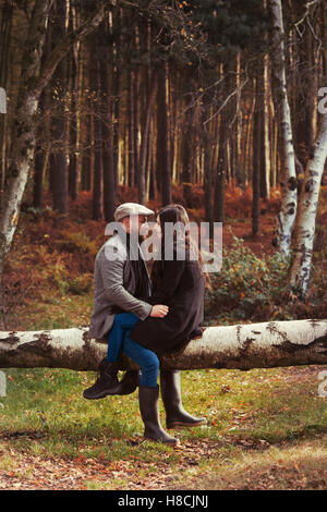 Young 30's couple sitting on a log in outdoor autumn setting in countryside Stock Photo
