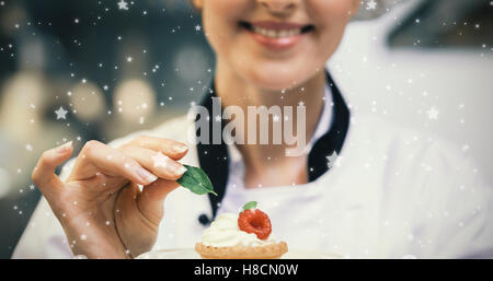 Composite image of smiling head chef putting mint leaf on little cake on plate Stock Photo