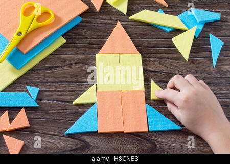 Hand baby rocket assembled figure in Tangram puzzle square wooden table above. The concept of early childhood development. Stock Photo