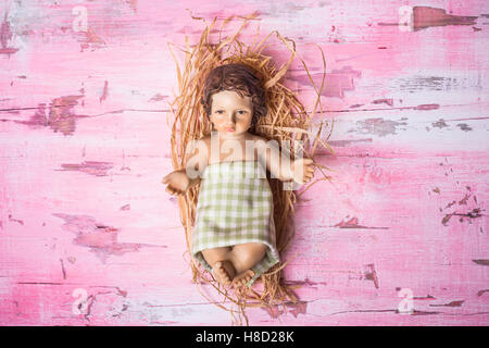 Baby Jesus Christmas card, cute figurine of Baby Jesus in his crib on rustic pink wooden background with empty space. Stock Photo