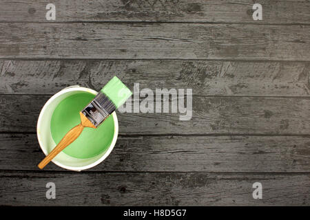 Loaded paintbrush placed across a white paint kettle filled with green paint on dark grey floor boarding Stock Photo