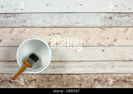 Loaded paintbrush placed across an empty white paint kettle on  light multicolored floor boarding Stock Photo