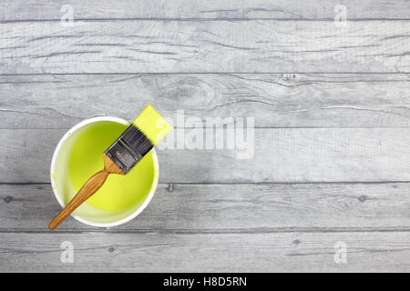 Loaded paintbrush placed across a white paint kettle filled with lime paint on a grey shabby style wood floor Stock Photo