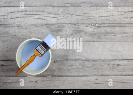 Loaded paintbrush placed across a white paint kettle filled with light blue paint on a grey shabby style wood floor Stock Photo