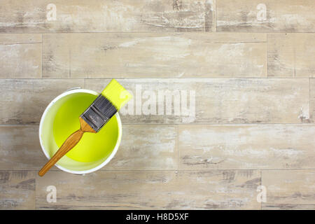 Loaded paintbrush placed across a white paint kettle filled with lime green paint on a shabby style wood floor Stock Photo