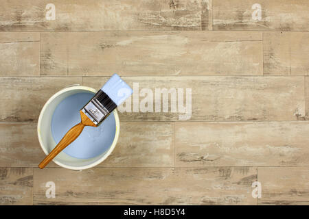 Loaded paintbrush placed across a white paint kettle filled with light blue paint on a shabby style wood floor Stock Photo