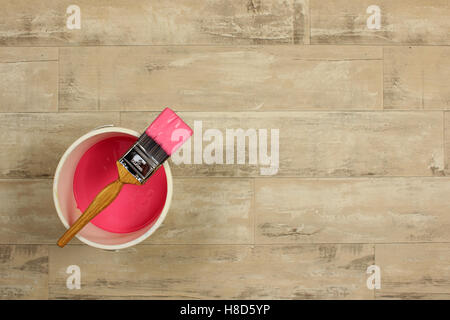 Loaded paintbrush placed across a white paint kettle filled with pink paint on a shabby style wood floor Stock Photo