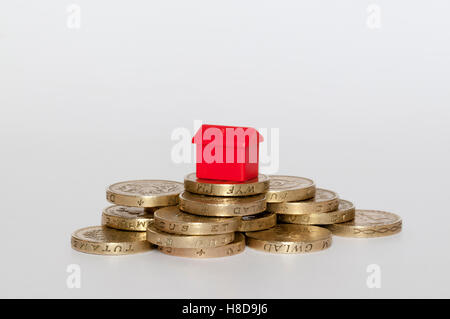 A small plastic model red house on top of a pile of pound coins.  Housing finance concept. Stock Photo