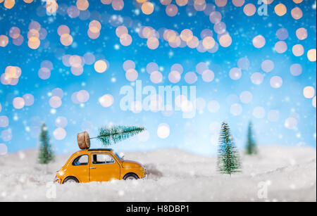 Miniature car carrying a Christmas tree in snow. Concept of Christmas Stock Photo