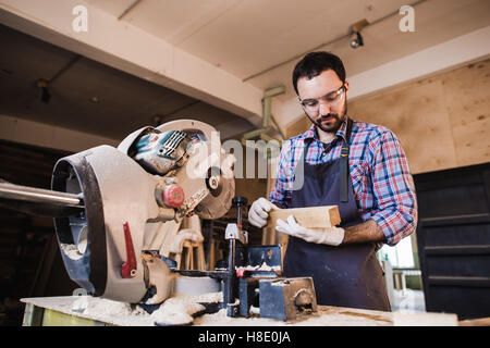 Carpenter working on an electric buzz saw cutting some boards, he is wearing safety glasses Stock Photo