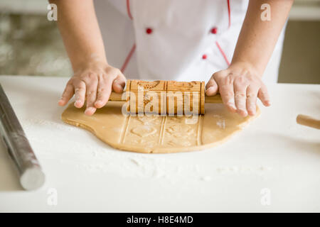 Close up of hands rolling gingerbread dough with patterned rolle Stock Photo