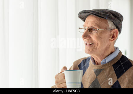 Elderly man holding a cup and looking through a window Stock Photo