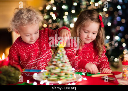 Little boy and girl making Christmas gingerbread house at fireplace in decorated living room. Kids playing with ginger bread Stock Photo