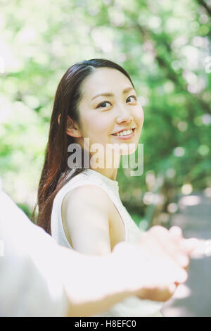 Young Japanese woman holding man's hand and smiling in a city park Stock Photo