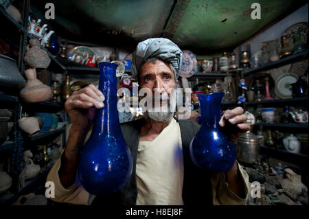 A glass blower holds up blue glass gourd-shaped vases in a trinket shop in Herat, Afghanistan, Asia Stock Photo