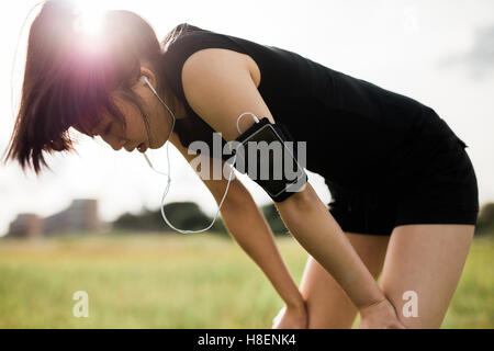 Tired young woman leaning over in sports gear. Sportswoman taking break from running workout at a park in morning.