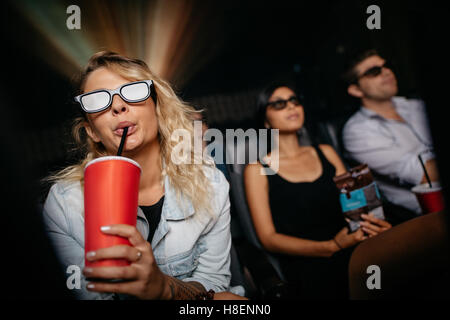 Young woman having cold drink wearing 3d glasses and watching movie in theater. People in cinema watching 3d film. Stock Photo