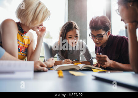 Group of young students working on school assignment in library. Multiethnic young people sitting at table reading reference boo Stock Photo