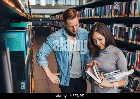Young people in library reading something in a book. Students choosing a book in a library. Stock Photo