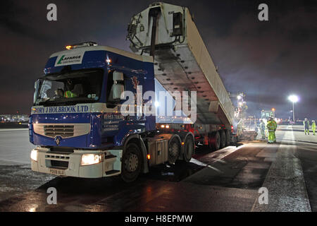 A lorry unloads asphalt into a road surfacing machine during the overnight resurfacing of Heathrow Airport's South Runway. London, UK Stock Photo