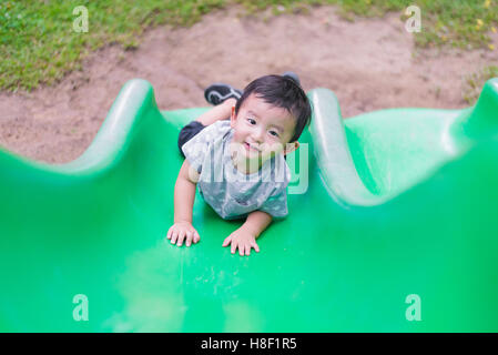 Little Asian kid climbing up the slide at the playground under the sunlight in summer, Kids play on school yard. Happy kid Stock Photo