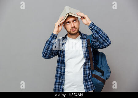 Young bearded male student with open book on his head having fun isolated on a gray background Stock Photo