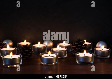 Tea lights with pine cones and baubles on a wooden surface, with copy space. Stock Photo