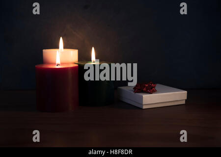 Three candles on a wooden surface with white gift box topped with a red ribbon. Stock Photo