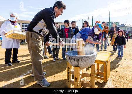 Japan. Omochi, winter rice bashing festival. Man holding with both hands a wooden mallet, a kine, while beating rice in usu, bowl. Outdoors. Stock Photo