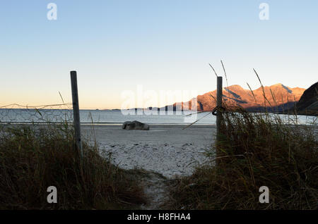 small trail and gate in front of white beach sand with ocean and mountain background Stock Photo