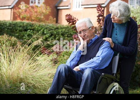 Depressed Senior Man In Wheelchair Being Pushed By Wife Stock Photo