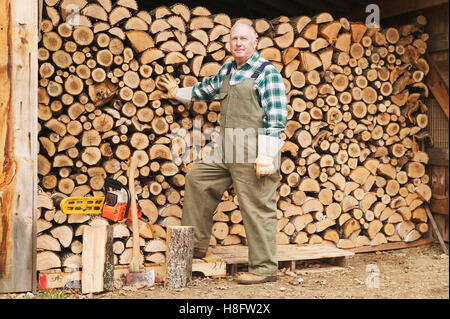 Senior man standing beside his wood pile Stock Photo